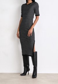 Sukienka o średniej długości w czarno-białe wzory, z krótkimi rękawami i rozcięciami po bokach, zestawiona z wysokimi na kolano czarnymi skórzanymi botkami na obcasie. Gładka faktura.