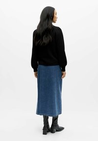 Pull noir à manches bouffantes associé à une jupe midi en jean bleu et des bottes à talons noires. Le tissu est lisse avec une légère brillance.