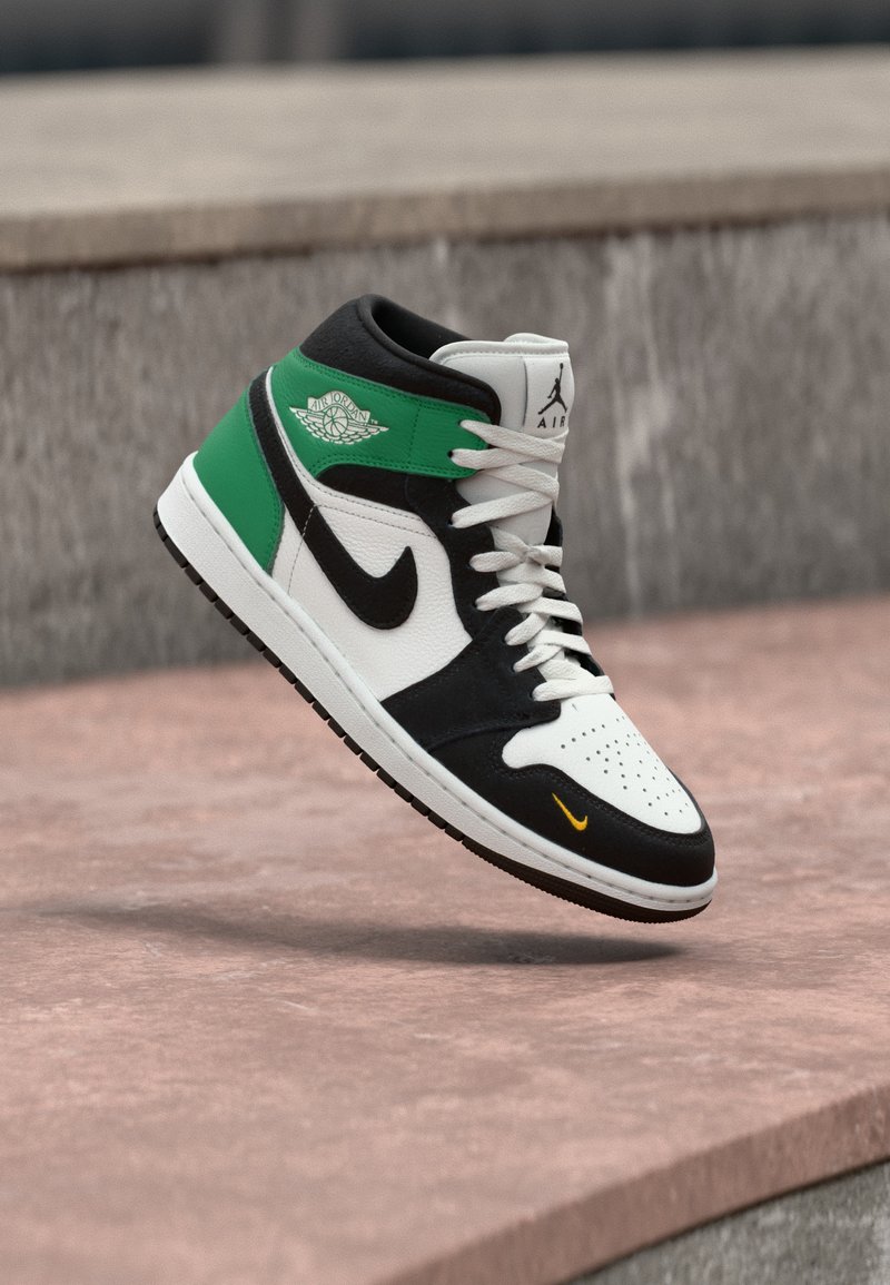 Unisex παπούτσι Air Jordan high-top σε λευκό, μαύρο και πράσινο, αιωρείται πάνω από μια ροζ πέτρινη επιφάνεια με γκρι φόντο.