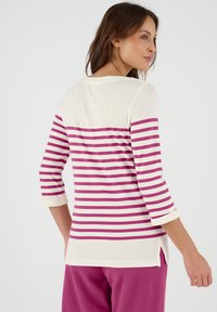 Gestreepte langemouwen top in crème en fuchsia. Heeft 3/4 mouwen, zijsplitten aan de onderkant en een ronde halslijn. Zachte stoftextuur.