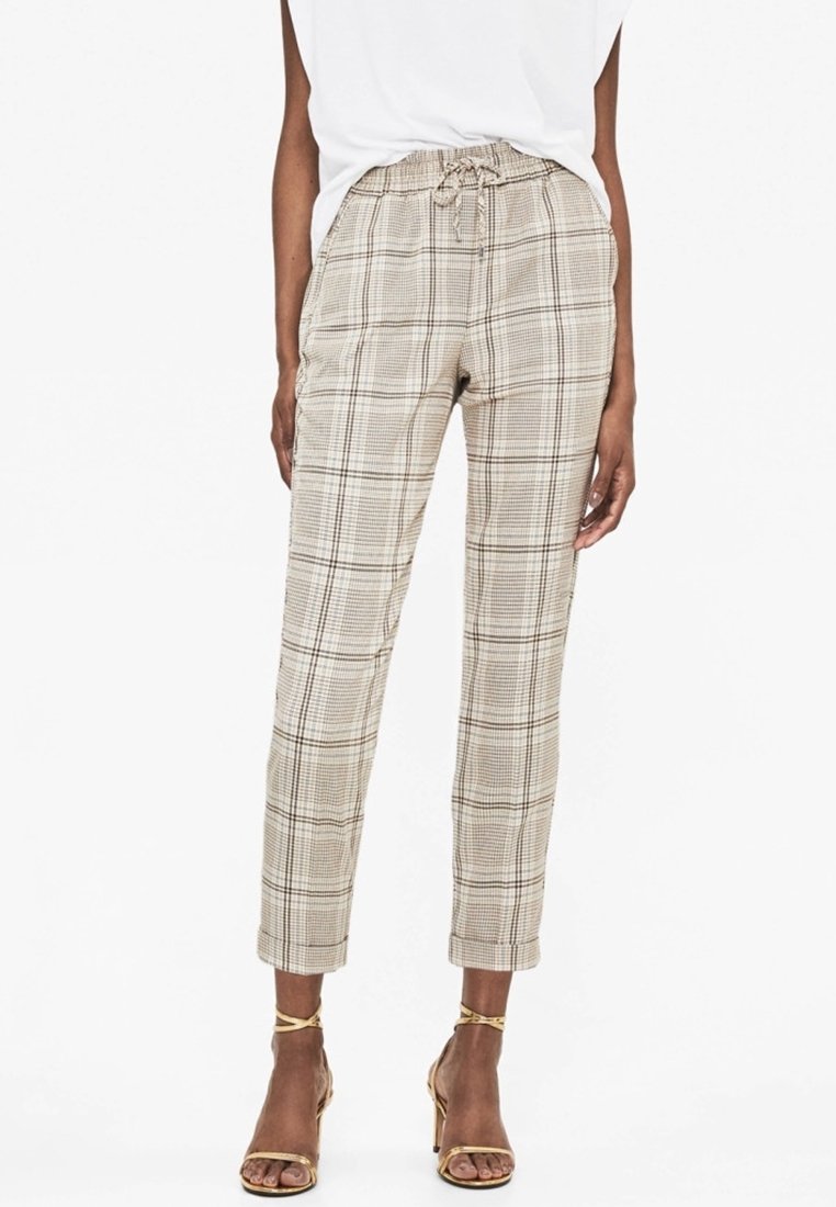 Pantalons à carreaux beiges avec une taille élastique et un cordon de serrage, présentant une jambe cintrée et des poignets retroussés. Tissu lisse et léger.