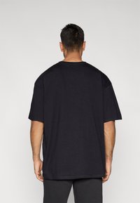 Fekete, rövid ujjú póló laza szabással és kerek nyakkivágással. Az anyag puha hatású, egyszínű, minták vagy díszítések nélkül.