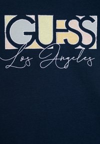 Camiseta navy con texto bordado multicolor de "GUESS Los Ángeles" en diferentes fuentes y estilos, con una textura de tela suave.