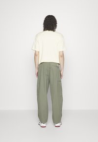 Camiseta de manga corta de color amarillo claro combinada con pantalones de pierna ancha verde oliva. Los pantalones cuentan con un bolsillo lateral y un ajuste relajado.