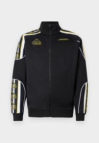 Black track jacket with high collar, full zipper, and yellow detailing. Features side stripes and logo accents on sleeves. Smooth fabric texture.