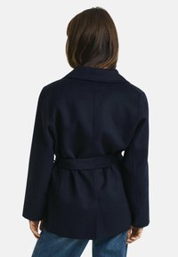 Marineblauwe wollen blend met riem, met een geknikte kraag, lange mouwen en een gestructureerde afwerking, met een gestroomlijnde silhoutte en zijsplitten.