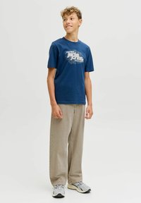 Camiseta de algodón azul marino con diseño gráfico blanco, acompañada de pantalones holgados marrón claro y zapatillas grises con detalles negros.