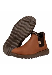 Botas de tobillo de cuero marrón con paneles laterales elásticos, suela de goma texturizada y banda de rodadura con patrón de olas. Cuenta con un parche de logo en el lateral.