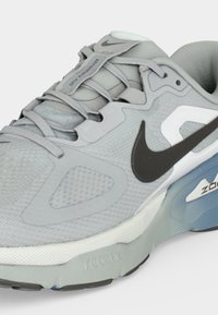 Ανοιχτό γκρι αθλητικό παπούτσι Nike με υφασμάτινο δίχτυ, κλείσιμο με κορδόνια, μαύρο λογότυπο Swoosh και μπλε σόλα με επένδυση και σήμανση "Zoom".
