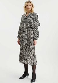 Zwart-wit geblokte jurk met een cowl halslijn, lange mouwen en een middellange rok. Geverfd stof en aansluitende taille accentueren de vorm.