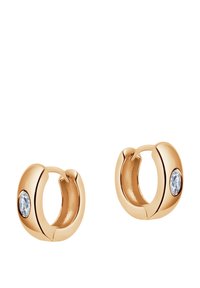 Kolczyki w kształcie kół w złotym odcieniu z małym, przezroczystym akcentem z kamienia szlachetnego po jednej stronie. Gładka, wypolerowana powierzchnia z zaokrąglonymi krawędziami.