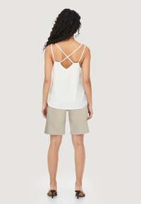 Witte mouwloze top met gekruiste banden en een open rug, gecombineerd met beige shorts en zwarte hakken. Glad materiaal, casual ontwerp.