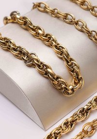 Gouden kettinghalsketting met vergrendelde ovale en ronde schakels, weergegeven op een glad, beige satijnen oppervlak.