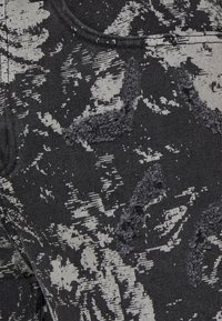 Distressed black denim fabric featuring a grey floral pattern. Texture shows frayed areas and varying fabric thickness in design.