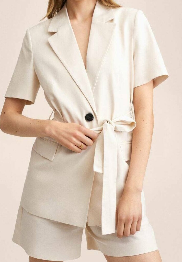 Blazer beige à manches courtes avec une taille à nouer, col à revers, deux poches avant et une fermeture à bouton noir unique ; associé à un short assorti.
