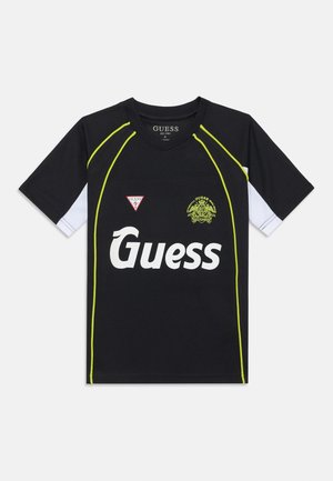 Maillot de sport noir avec de courtes manches blanches, accents vert fluo, et un grand logo "Guess" blanc. Présente un logo triangulaire sur le côté gauche.