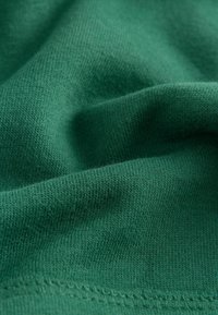 Tessuto di cotone verde con una trama morbida, caratterizzato da un sottile motivo a maglia e cuciture visibili lungo il bordo.