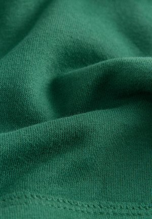 Vihreä kangas, jossa on pehmeä, teksturoitu jersey-kutominen. Lähellä otettu kuva näyttää hienoja, tasaisia ompeleita ja sileän pinnan.