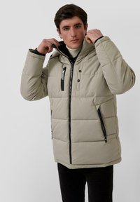 Bežinis pūkinis švarkas su tekstūruotu paviršiumi, turintis užtrauktuką priekyje, gobtuvą ir dvi užtrauktukais uždaromas kišenes. Juodi akcentai aplink užtrauktukus.