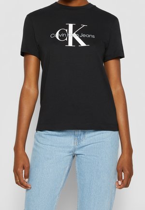 Black cotton t-shirt featuring a white Calvin Klein logo and graphic design. Short sleeves and a relaxed fit, paired with light blue jeans.