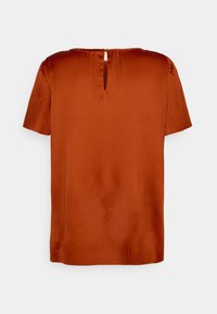 Top de mangas curtas em laranja enferrujado, feito de tecido suave com uma textura em ribete. Apresenta um pequeno corte em forma de chave na parte de trás do decote.