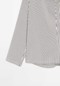 Gestreifte Bluse mit schmalen schwarzen und weißen vertikalen Streifen, aus leichtem Stoff, mit langen Ärmeln und abgerundetem Saum.