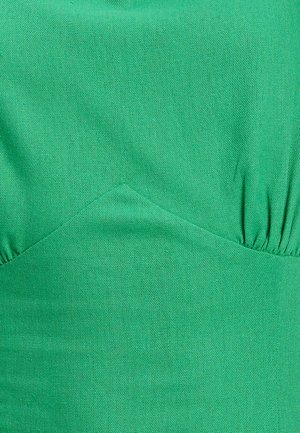 Tejido verde con una textura suave, que presenta un diseño ajustado y detalles fruncidos a los lados. El color es vibrante y uniforme en todo.