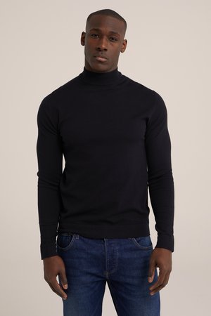Schwarzer Rollkragenpullover aus glattem Strickmaterial mit langen Ärmeln und taillierter Passform. Kombiniert mit blauen Jeans.