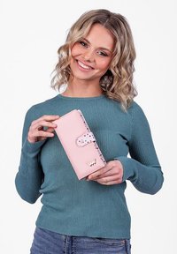 Pink faux leather wallet with a snap closure, white and colored dot accents, and a gold logo. Model holds it against a plain background.