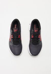 Črne športne copate z rdečimi akcenti, mrežastim zgornjim delom, teksturirano površino, okroglo konico in črnimi vezalkami, ki imajo belo podplato in logo na jeziku.