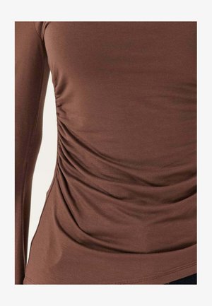 Brun langærmet tætsiddende skjorte med rynkedetalje i siden på en persons overkrop, der viser stoffets tekstur og fald.