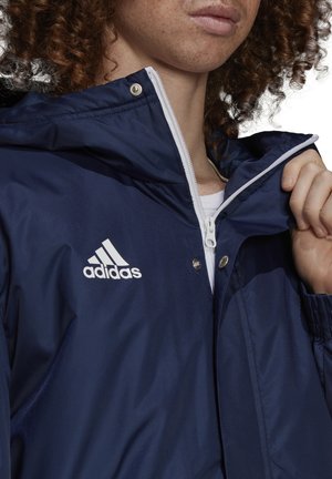 Marineblauer Windbreaker mit Reißverschluss und Druckknöpfen, ausgestattet mit einem weißen Adidas-Logo auf der Brust und kontrastierenden weißen Reißverschlüssen.