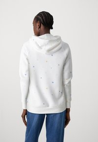 Sudadera blanca con patrones de estrellas multicolores, textura suave, mangas largas y un corte relajado. Cuenta con capucha con cordón y dobladillo acanalado.