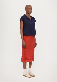 Marineblå crop-top med korte ermer og krage, kombinert med et rødt skjørt med volangkant. Beige sneakers fullfører antrekket.