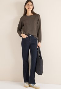 Brown textured long-sleeve top, dark blue flared jeans, white sneakers with blue accents, and a black bag held in one hand.