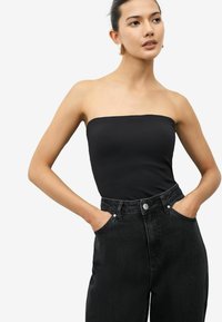 Svart axelbandslös topp i slät tyg, matchad med högmidjade, mörk denimjeans med sidofickor och knappstängning.