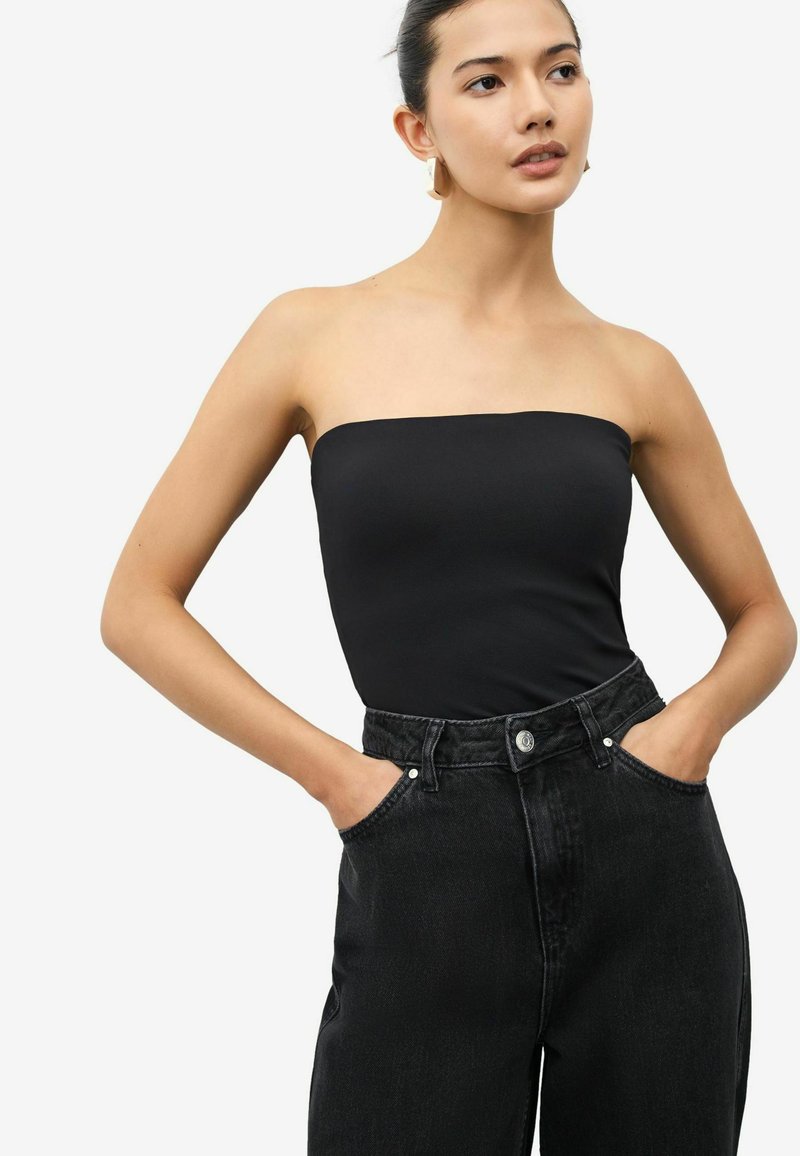 Svart axelbandslös topp i slät tyg, matchad med högmidjade, mörk denimjeans med sidofickor och knappstängning.