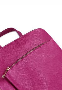 Felroze leren rugzak met textuur, voorzien van een voorzak met rits en bijpassende handvatten op een witte achtergrond.