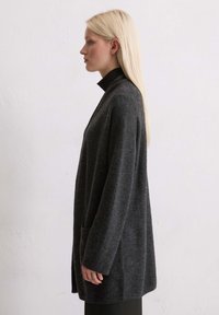 Szary, długi kardigan z wysokim kołnierzem, wykonany z miękkiego materiału, z kieszenią z przodu i luźnym krojem. Gładka tekstura, minimalistyczny design.