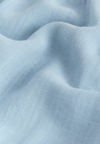 Tissu tissé bleu clair avec une texture visible et de doux plis créant des ombres et des reflets délicats.