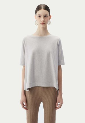 Light gray short-sleeve sweater with a relaxed fit and side slits, paired with ribbed brown leggings. Smooth texture, simple design.