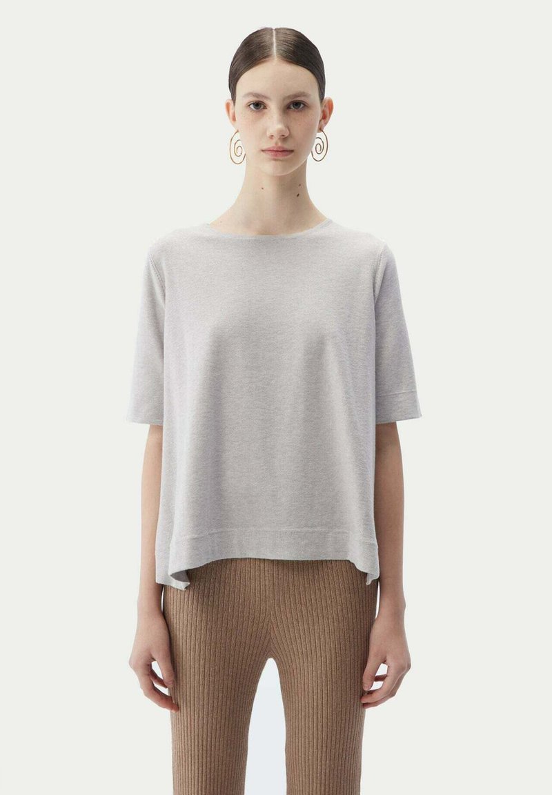 Ljusgrå kortärmad tröja med avslappnad passform och sidöppningar, i kombination med bruna leggings med ribbad struktur. Slät textur, enkelt mönster.