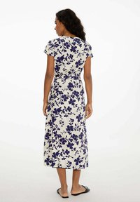 Kvetinové zavinovacie šaty v krémovej farbe s námořníckym modrým vzorom kvetov, krátke rukávy, dĺžka po členky, s viazaním v páse a hladkou textúrou látky.
