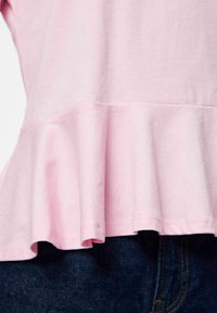 Lyserosa peplumtopp med myk tekstur, med utsvingt kant, lagdelte volanger, og kombinert med mørke denimjeans.