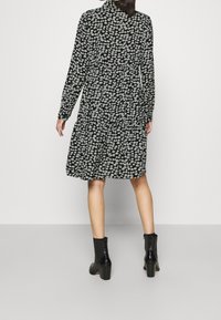 Abito nero con motivo floreale bianco, maniche lunghe, design a strati, scollatura tonda, abbinato a stivali neri alla caviglia, texture liscia.