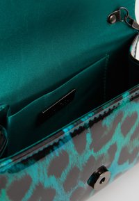 Borsa a tracolla con stampa leopardo teal e nera, con chiusura magnetica aperta, che mostra l'interno in tessuto teal liscia e una piccola tasca interna.