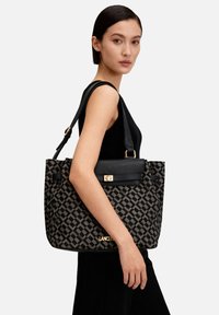 Borsa tote con motivo geometrico nero e grigio, con patta in pelle nera e dettagli dorati, dotata di due manici robusti e una forma strutturata.