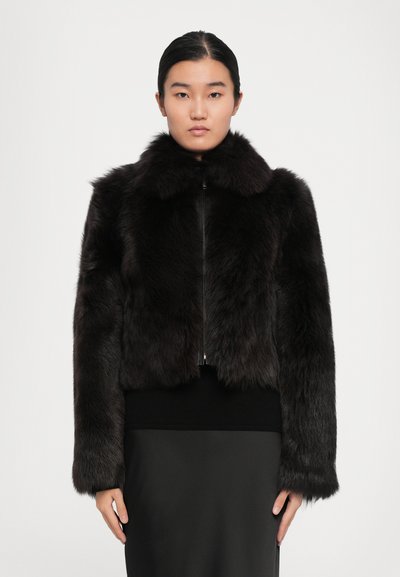 Veste cropped en fausse fourrure noire avec un col montant, fermeture éclair à l'avant et manches longues. Elle présente une texture douce et une silhouette ajustée.