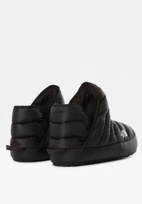 Zapatillas deslizables negras aislantes con textura acolchada, parte trasera redondeada y suela de goma. Con un logo en el lateral y un suave forro interior.