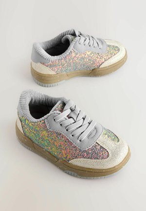 Een paar grijze sneakers met multicolor glitterpanelen, beige accenten, dikke zolen en grijze veters, geplaatst op een lichte ondergrond.